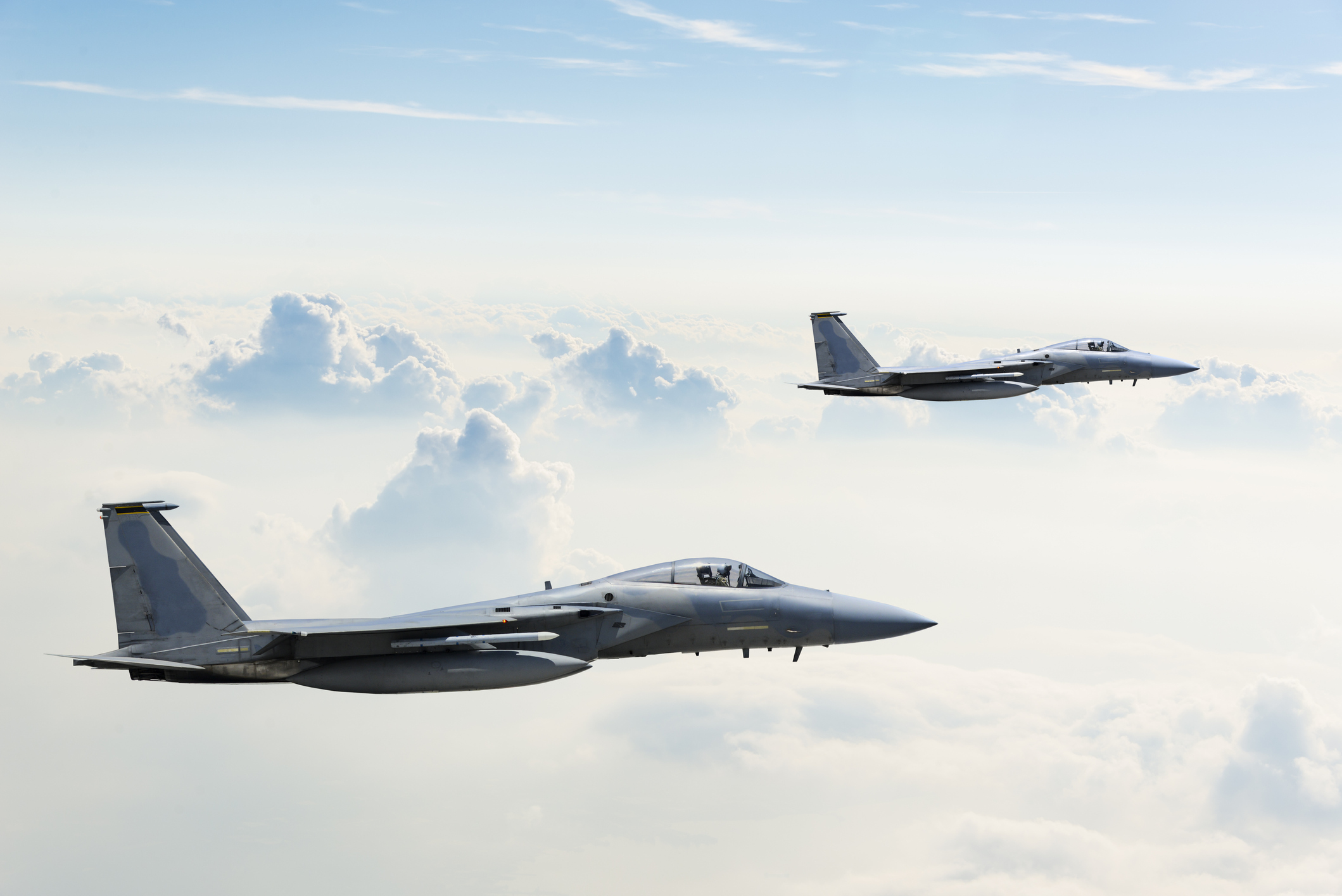 Two F-15 Eagle fighter jets flying above clouds